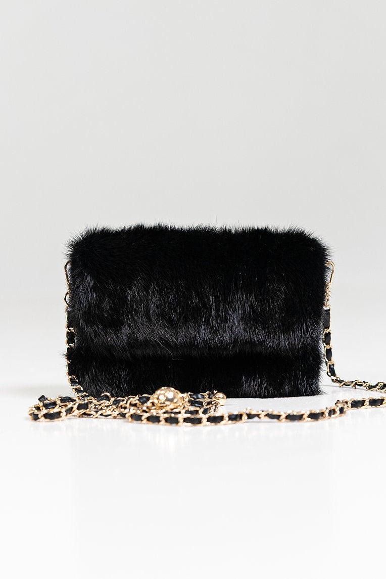 A black fur shoulder bag with a gold-tone chain strap, displayed on a clean white background.