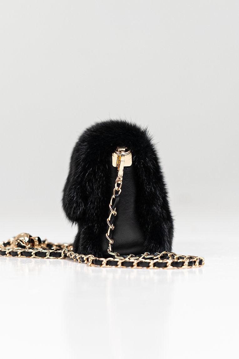 Black fur handbag with gold chain on a light gray background