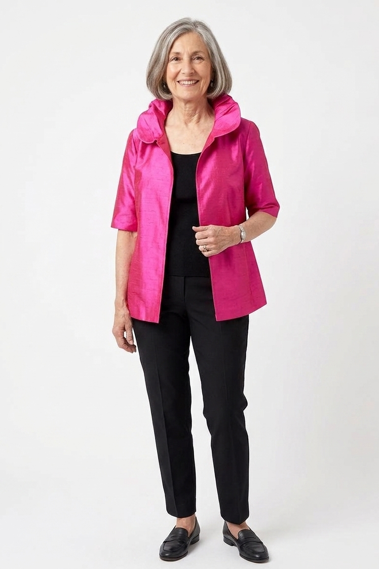 Woman wearing a bright pink jacket over a black top and pants on a white background
